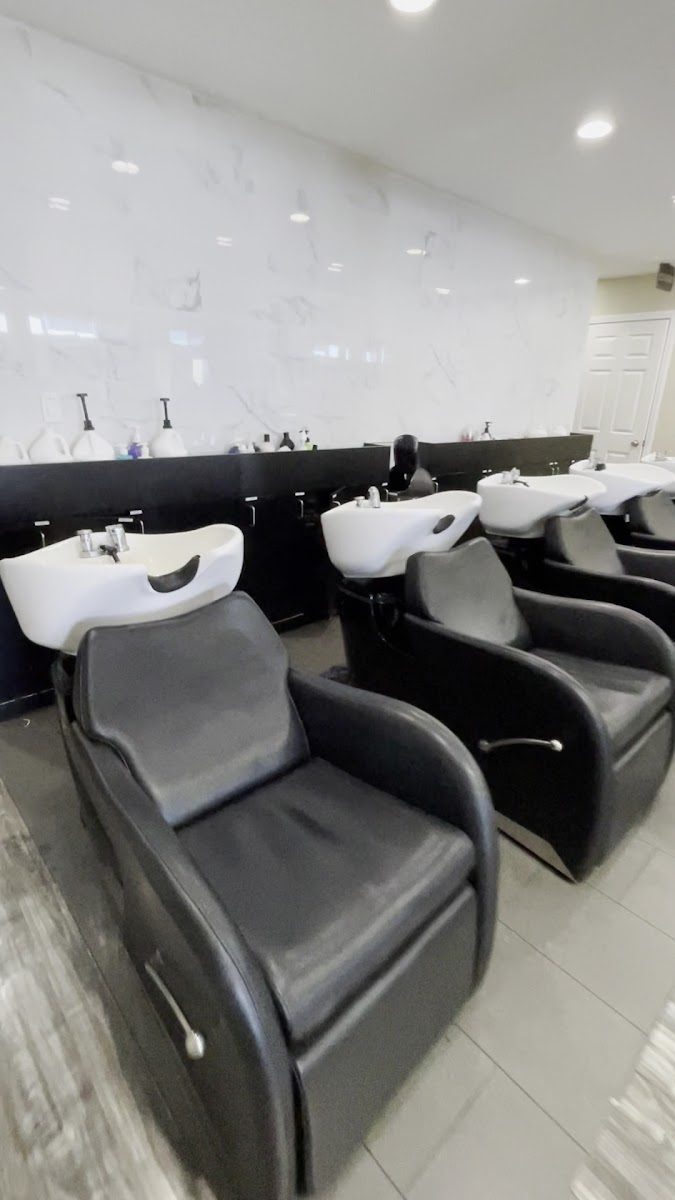A row of black reclining shampoo chairs with white basins against a marble-look wall